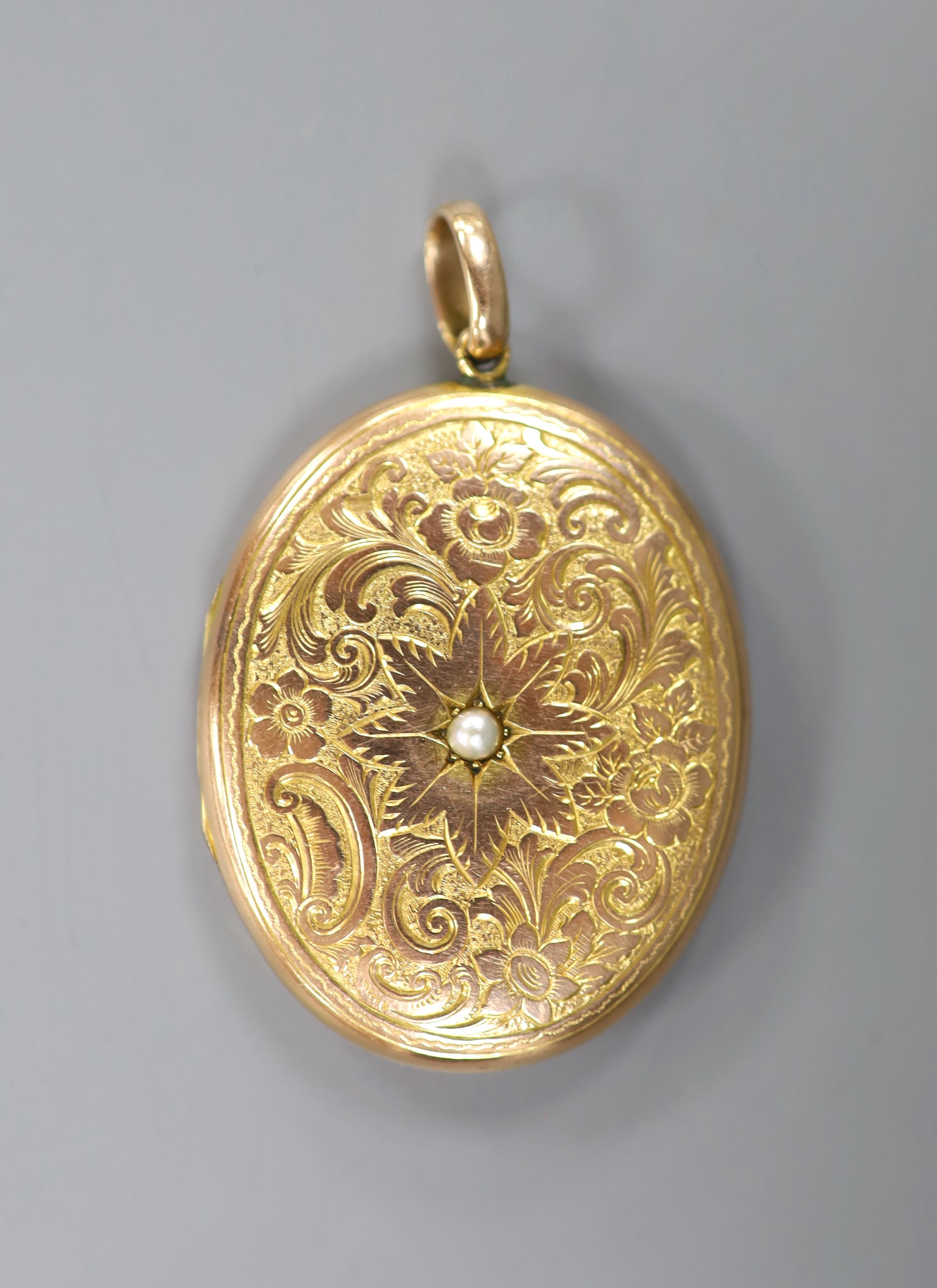 An early 20th century engraved yellow metal (stamped 9c) and split pearl set oval locket, 44mm, gross weight 13.5 grams, with engraved monogram.